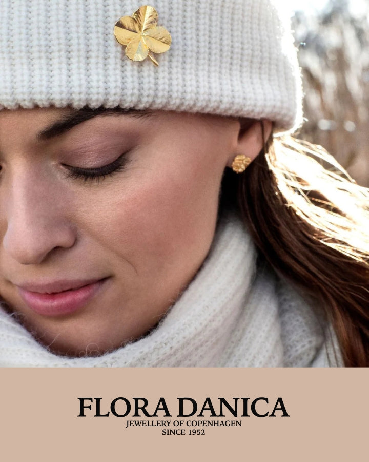 Flora Danica smykke kollektion, guldfarvet firkløver broche på hvid hue og ørestik, forsidefoto